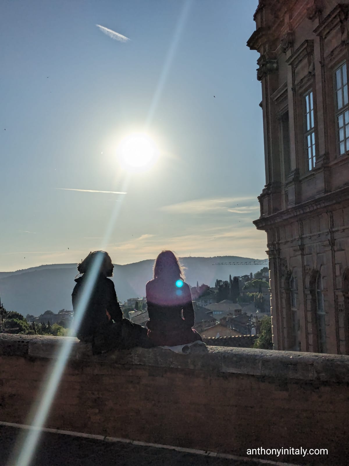 picture of a couple sitting on a wall with the bright sun behind them