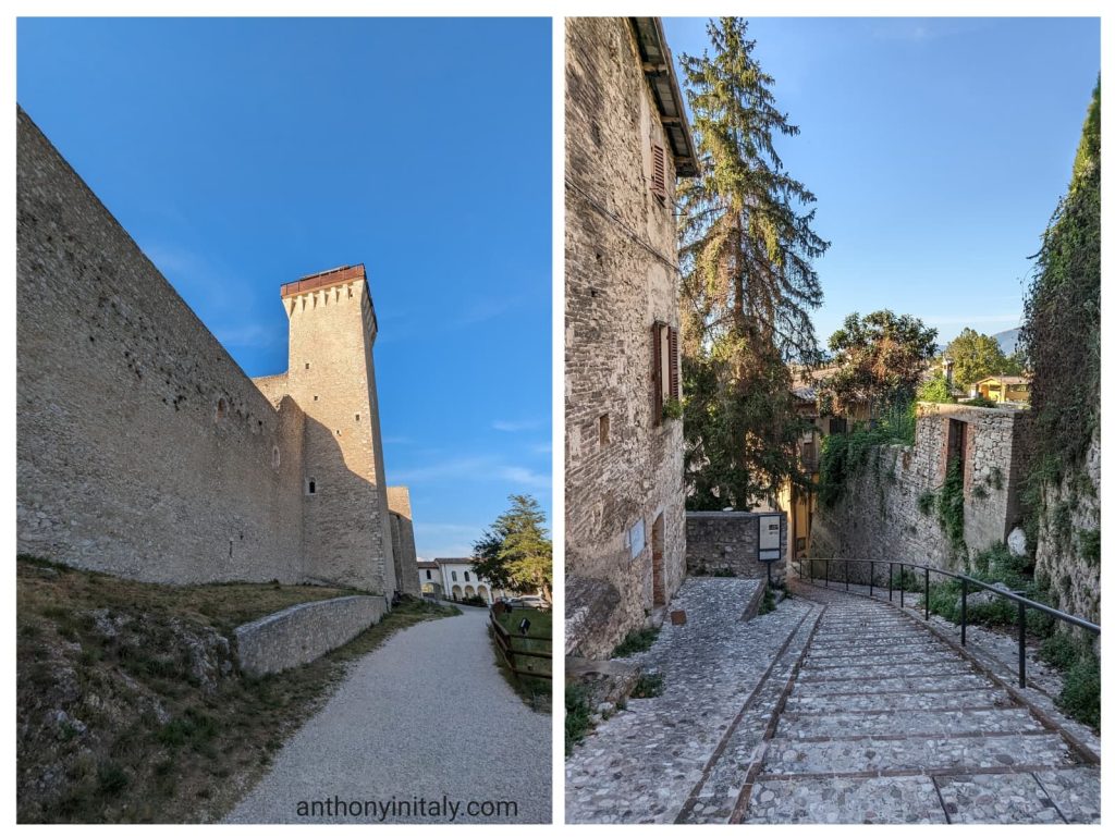Stone walls and tower of the Rocca Albornoz fortress in Spoleto under a clear blue sky, followed by a quiet cobblestone stairway descending through historic stone buildings surrounded by greenery