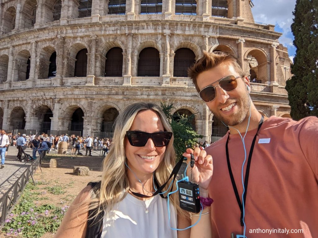 guy and girl standing in front of colosseum in rome with tour guide headsets on