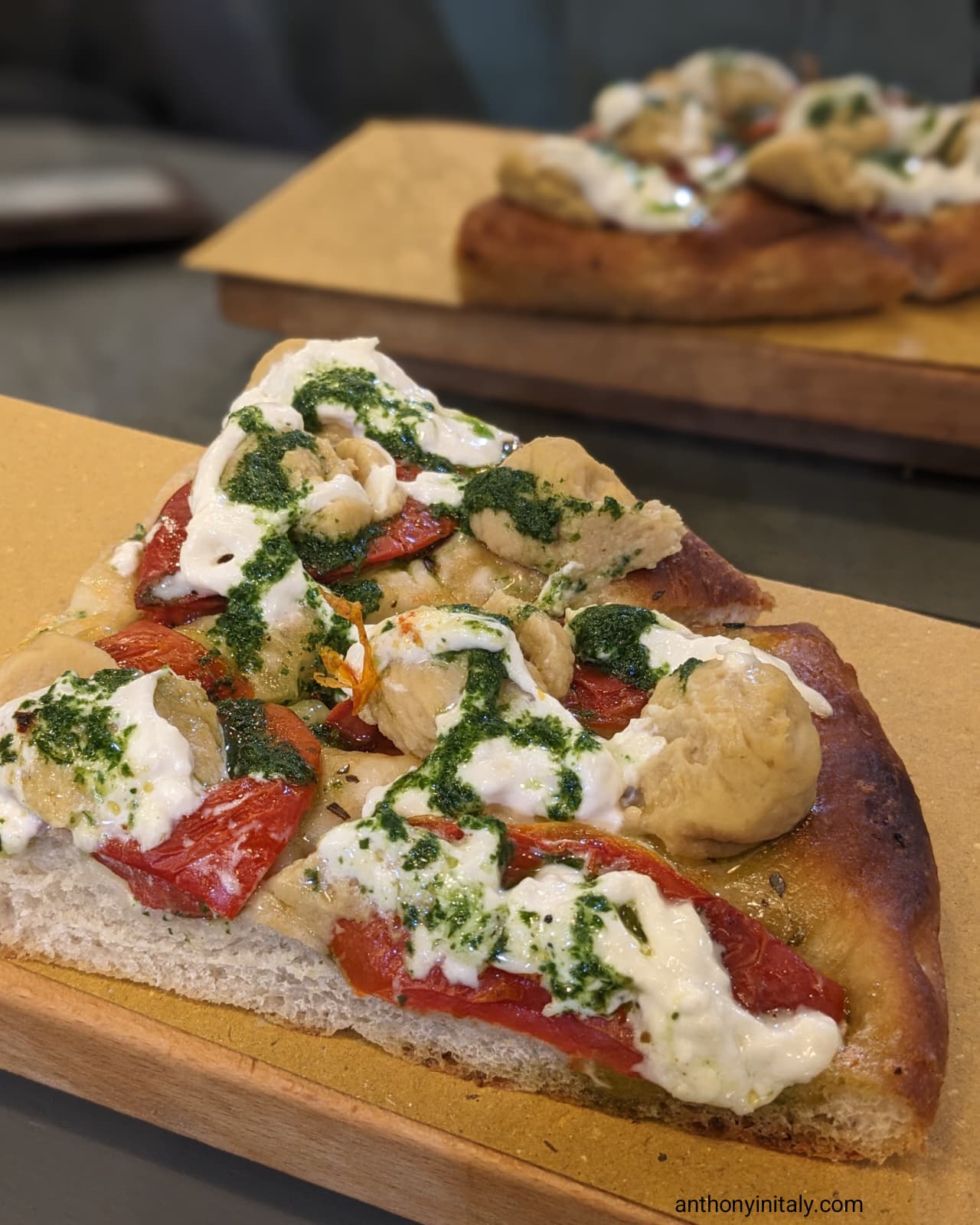 Close-up of a Pugliese-style focaccia slice from Mató in Rome, topped with roasted red peppers, stracciatella cheese, green herb pesto, and scoops of chickpea or eggplant puree.