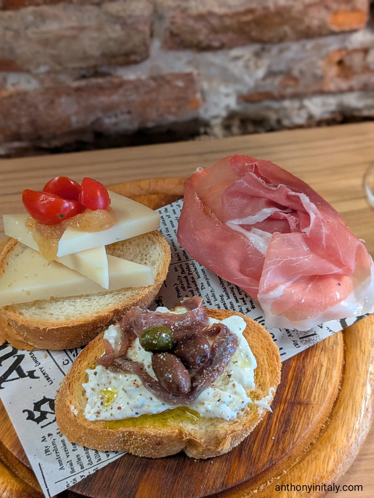 Trio of Udine crostini topped with cherry tomatoes and cheese, creamy stracciatella with anchovies and olives, and folds of prosciutto.