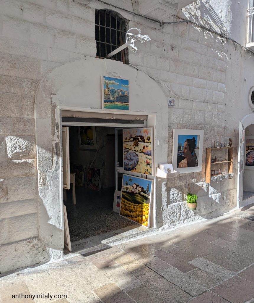 Small art shop at Via Barbacana 50 in Monopoli with hand-painted canvases at the entrance