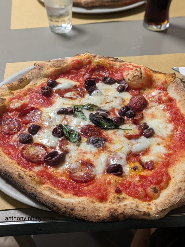Neapolitan-style diavola pizza with tomato, mozzarella, spicy salami, black olives, and basil on a puffy, leopard-spotted crust at Medì Pizzeria Mediterranea in Perugia