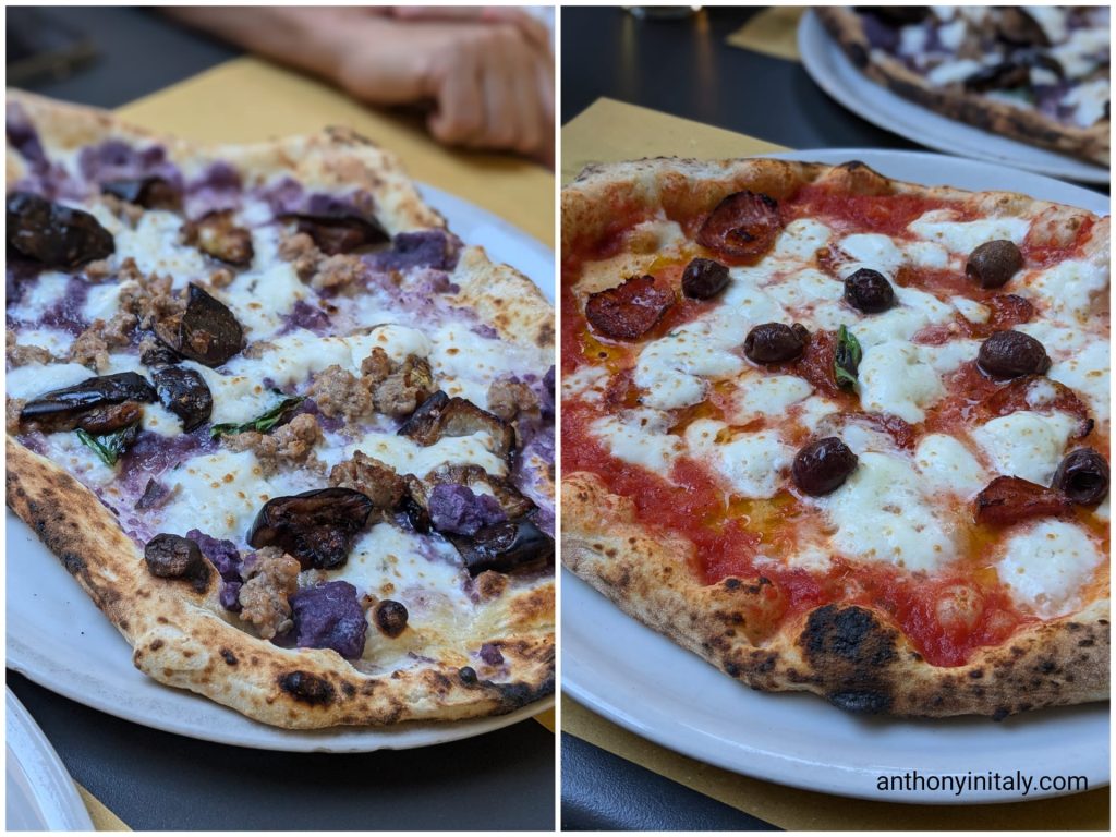 Neapolitan-style pizza with purple potato cream, sausage, eggplant, and mozzarella next to a diavola pizza with spicy salami and olives at Pizzeria Mediterranea Tre Archi in Perugia