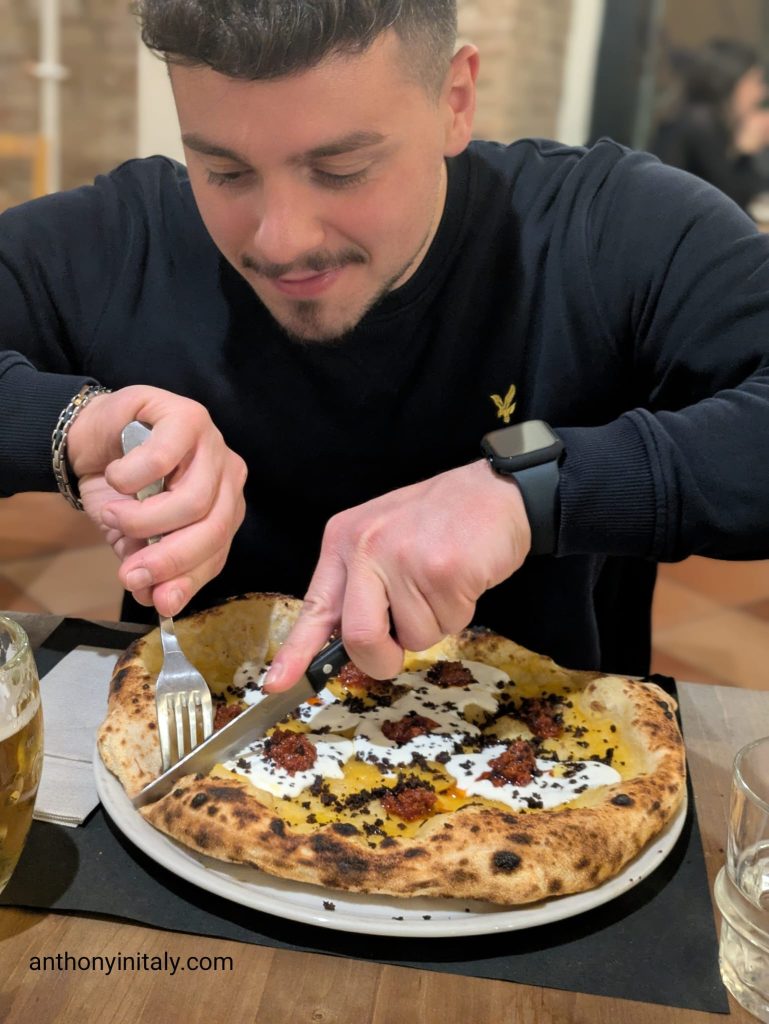 Diner cutting into a Neapolitan-style Calabrese pizza with ‘nduja, onion jam, olive powder, and a puffy charred crust at Verace in Perugia